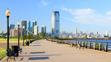 A waterfront promenade with benches and street lamps, leading to a city skyline with modern skyscrapers.