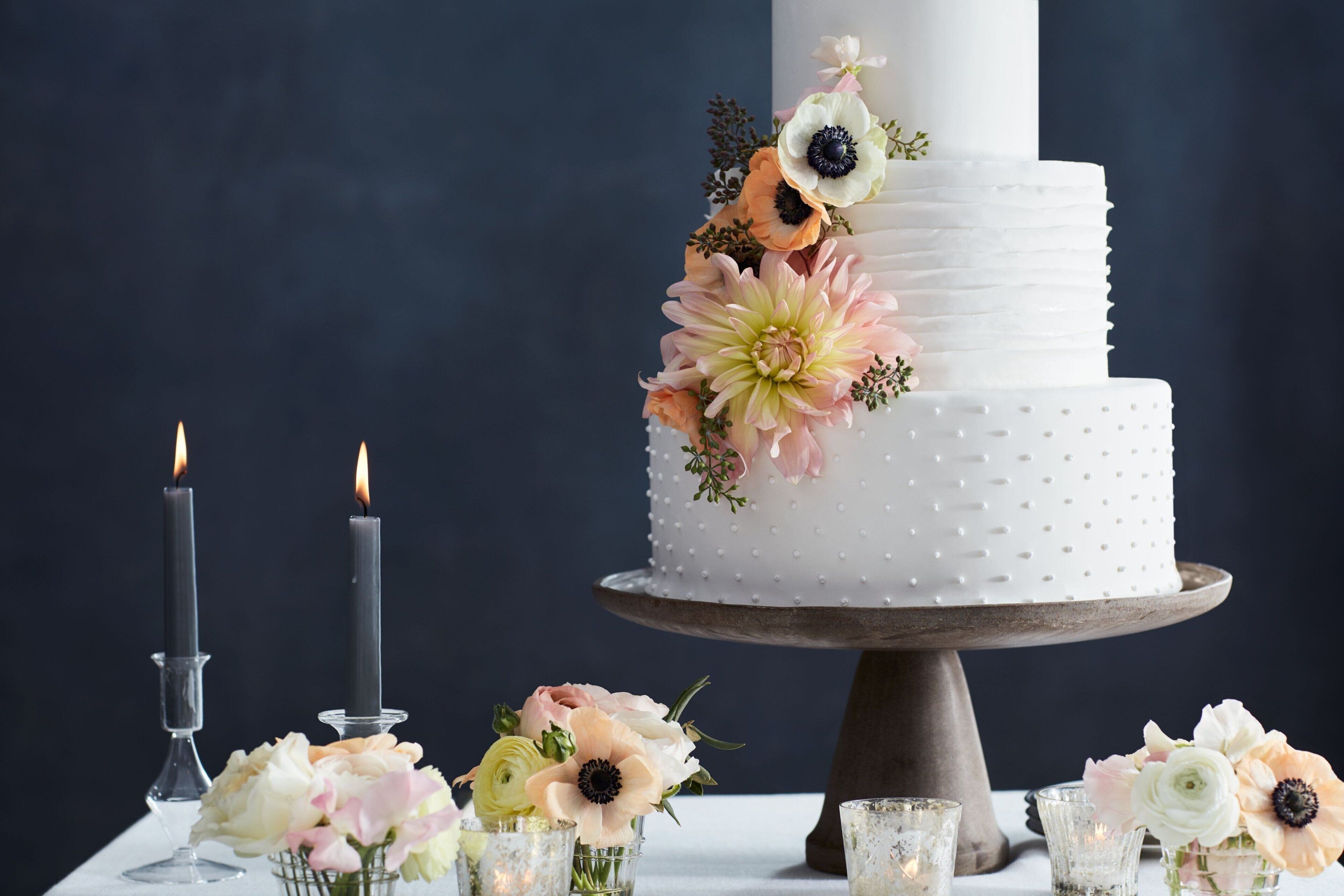 Un pastel blanco de varios niveles con decoraciones florales sobre un soporte de madera.