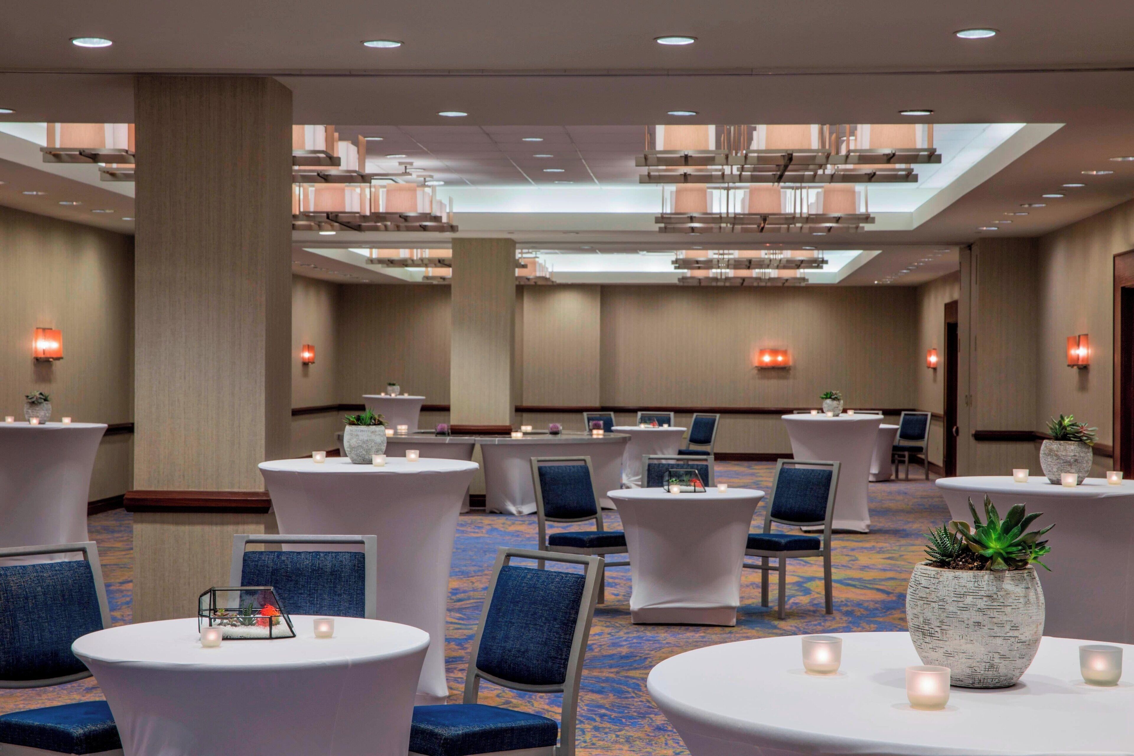 A hotel lobby with round tables, blue chairs, and potted plants.
