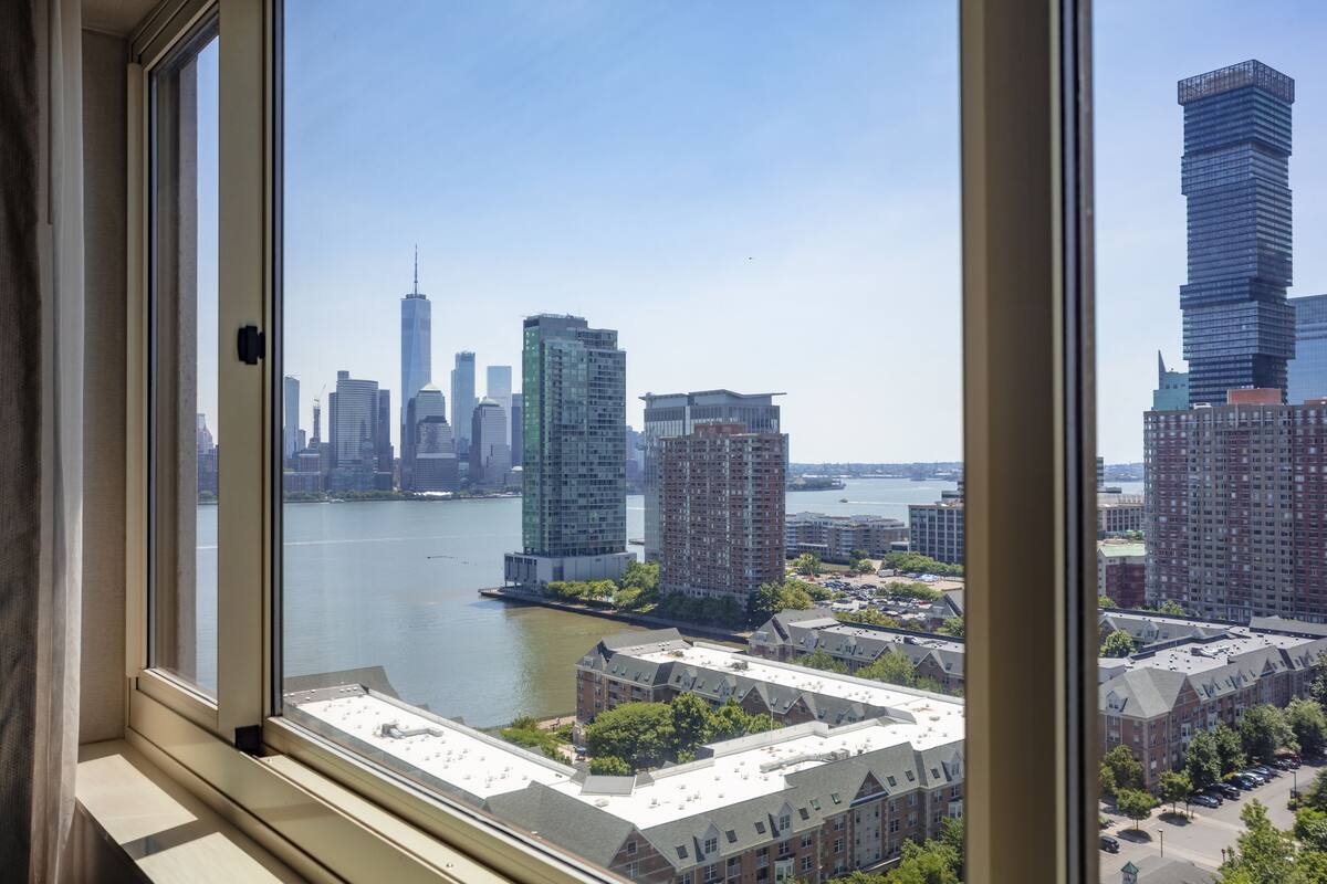 A view from a window overlooking a cityscape with high-rise buildings, a river, and a clear sky.