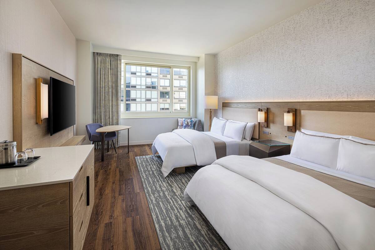 A hotel room with two beds, a desk, a TV, and a window with curtains.