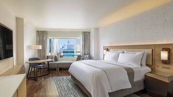Een hotelkamer met een groot bed, een bureau, een stoel, een klein tafeltje en uitzicht op de stad.