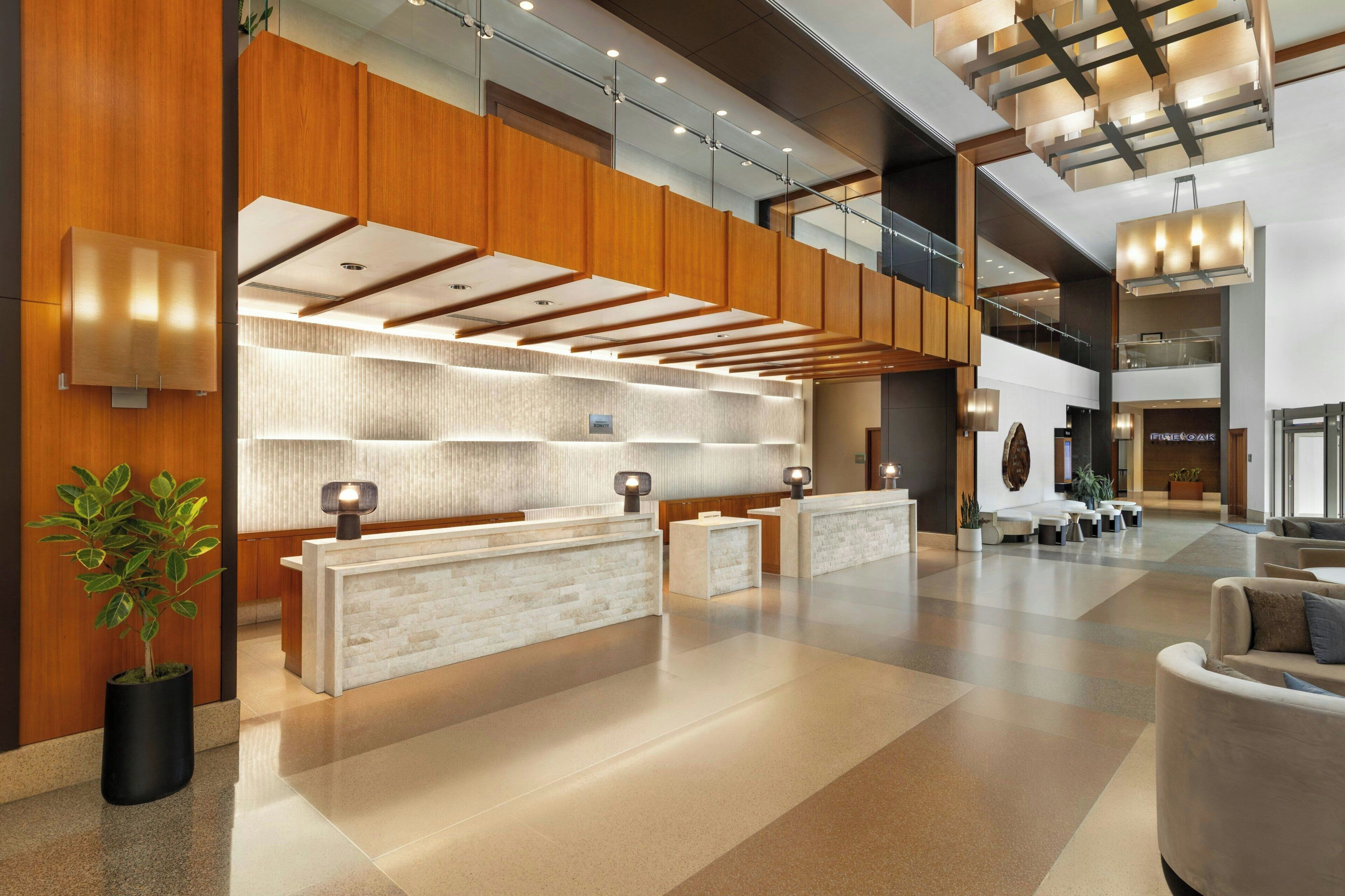 A modern hotel lobby with a reception desk, seating area, and a staircase leading to upper floors.