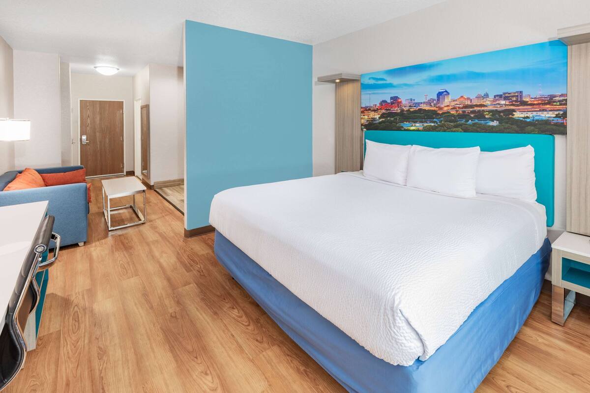 A hotel room with a large bed, a desk, a chair, and a cityscape painting on the wall.