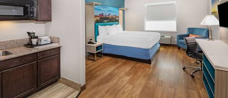Habitación de hotel con cama, escritorio, silla, microondas, tostadora y lavabo.