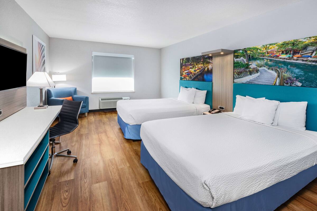 A hotel room with two beds, a desk, a chair, a TV, and a large window.