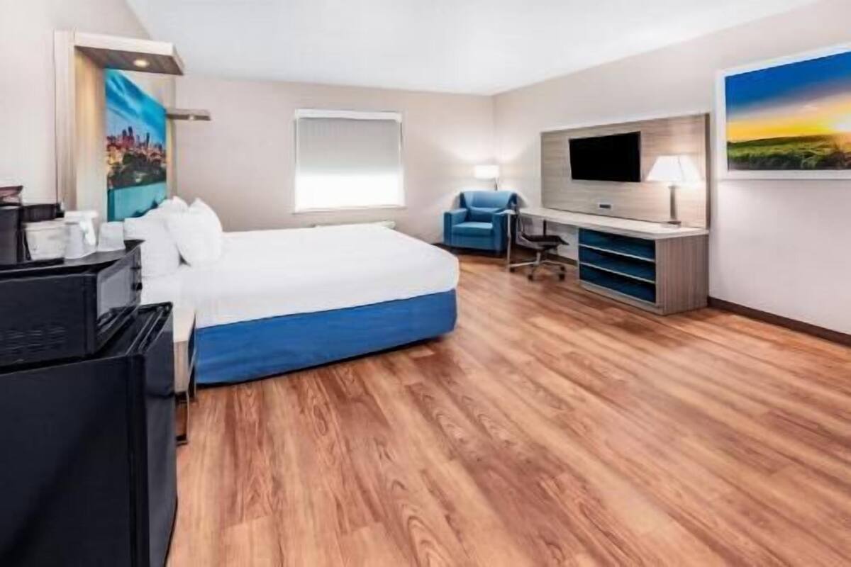 A hotel room with a bed, a desk, a chair, a TV, and a painting on the wall.