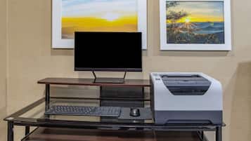 A desk with a computer monitor, keyboard, and printer. There are two framed pictures on the wall behind the desk.