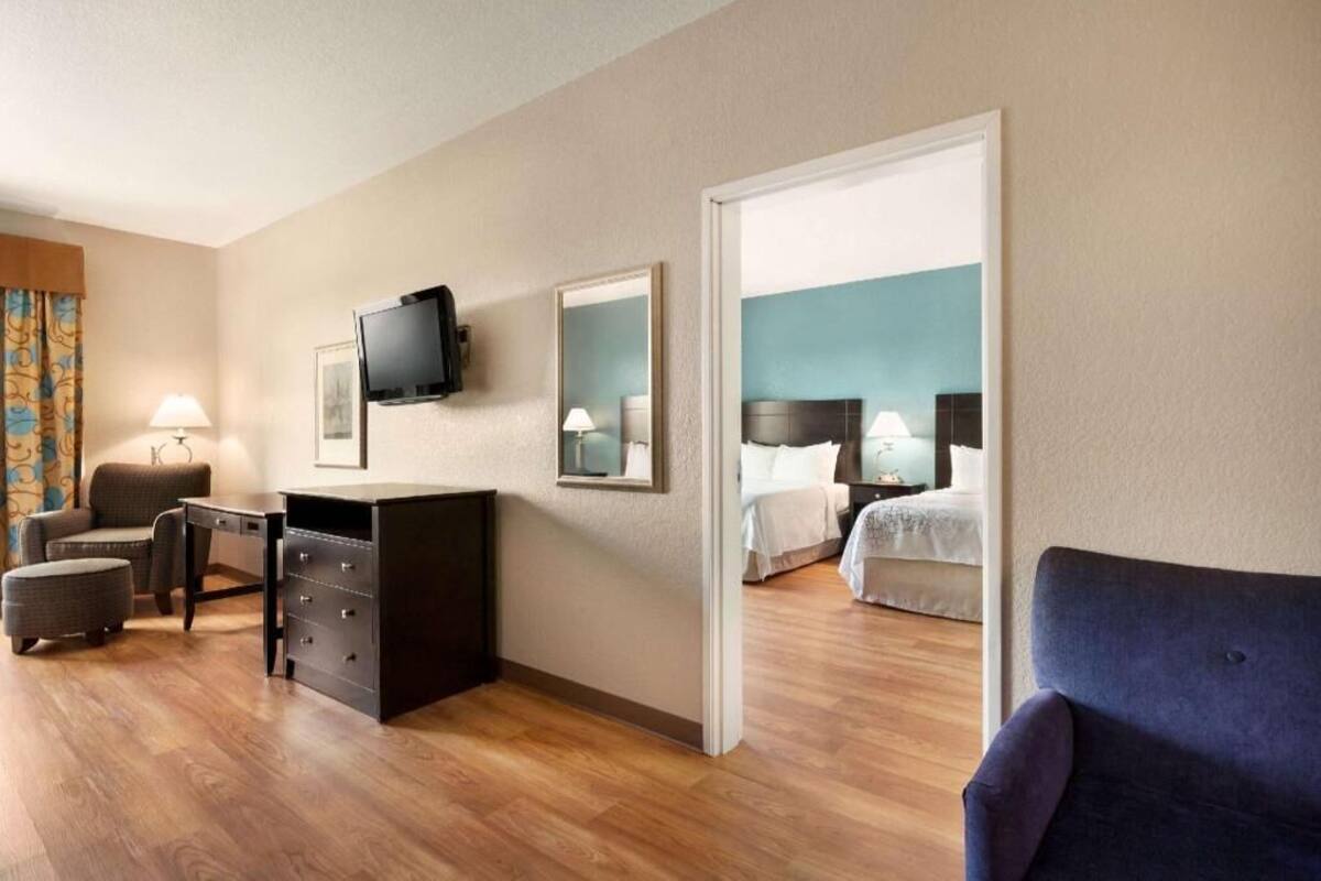 A hotel room with a desk, chair, television, two beds, and a large mirror.