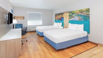 A hotel room with two beds, a desk, a chair, a TV, and a painting on the wall.