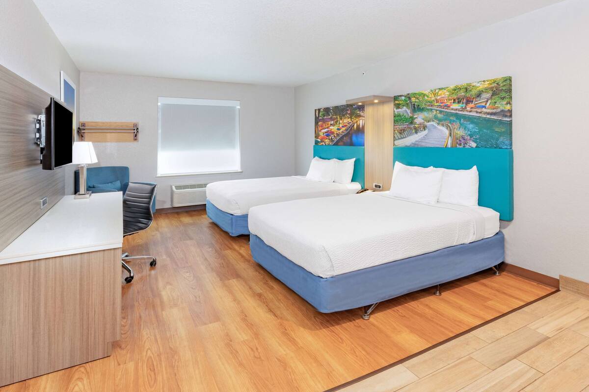 A hotel room with two beds, a desk, a chair, a TV, and a painting on the wall.