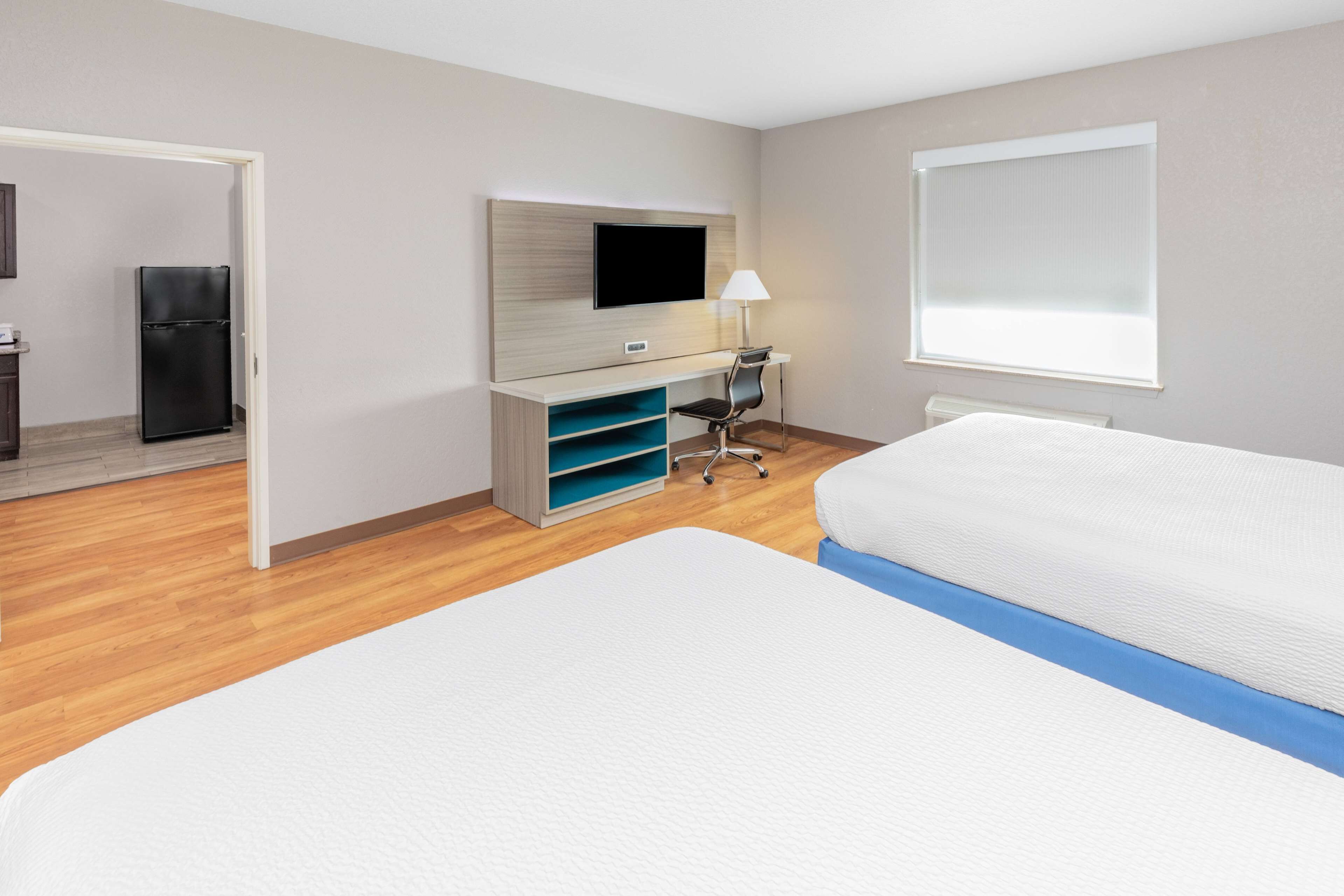 Habitación de hotel con cama, escritorio, silla, televisor, ventana y refrigerador.