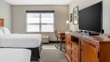 Quarto de hotel com duas camas, uma escrivaninha com TV de tela plana, uma cadeira e uma janela com persianas.