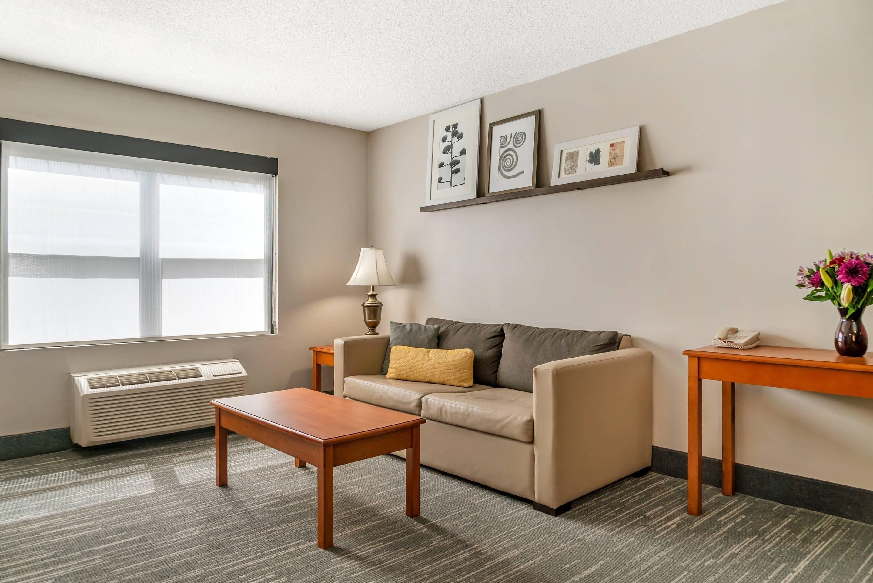 A furnished living room with a sofa, a coffee table, a lamp, a side table with a phone, and a window with blinds.