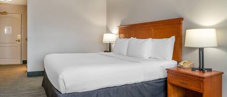 A hotel room with a large bed, bedside lamps, a nightstand with a phone, and a door with a lock.