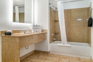 A modern bathroom with a granite countertop sink, a white bathtub, and a shower area with a granite wall.