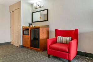 A hotel room with a red armchair, a minibar, a microwave, and a door.
