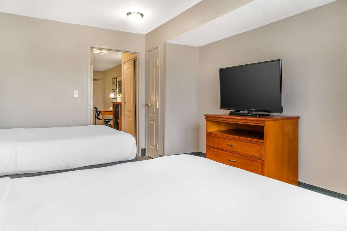 A hotel room with two beds, a television on a wooden stand, and a door leading to another room.