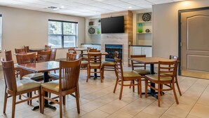 A dining area with wooden tables and chairs, a flat-screen TV mounted on the wall, and a fireplace.