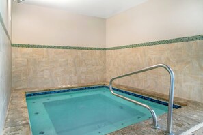 Piscina com guarda-corrimão de metal, rodeada por paredes revestidas de azulejos bege e borda em mosaico verde e azul.