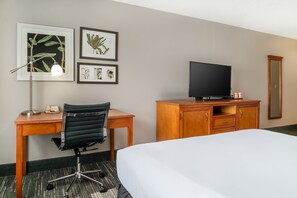 A hotel room with a bed, desk, chair, television, and framed botanical artwork on the wall.