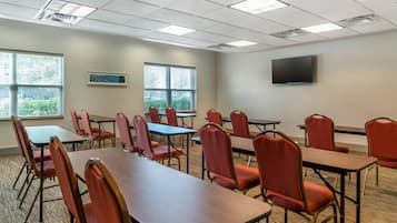 A conference room with tables and chairs, a flat-screen TV on the wall, and windows with blinds.