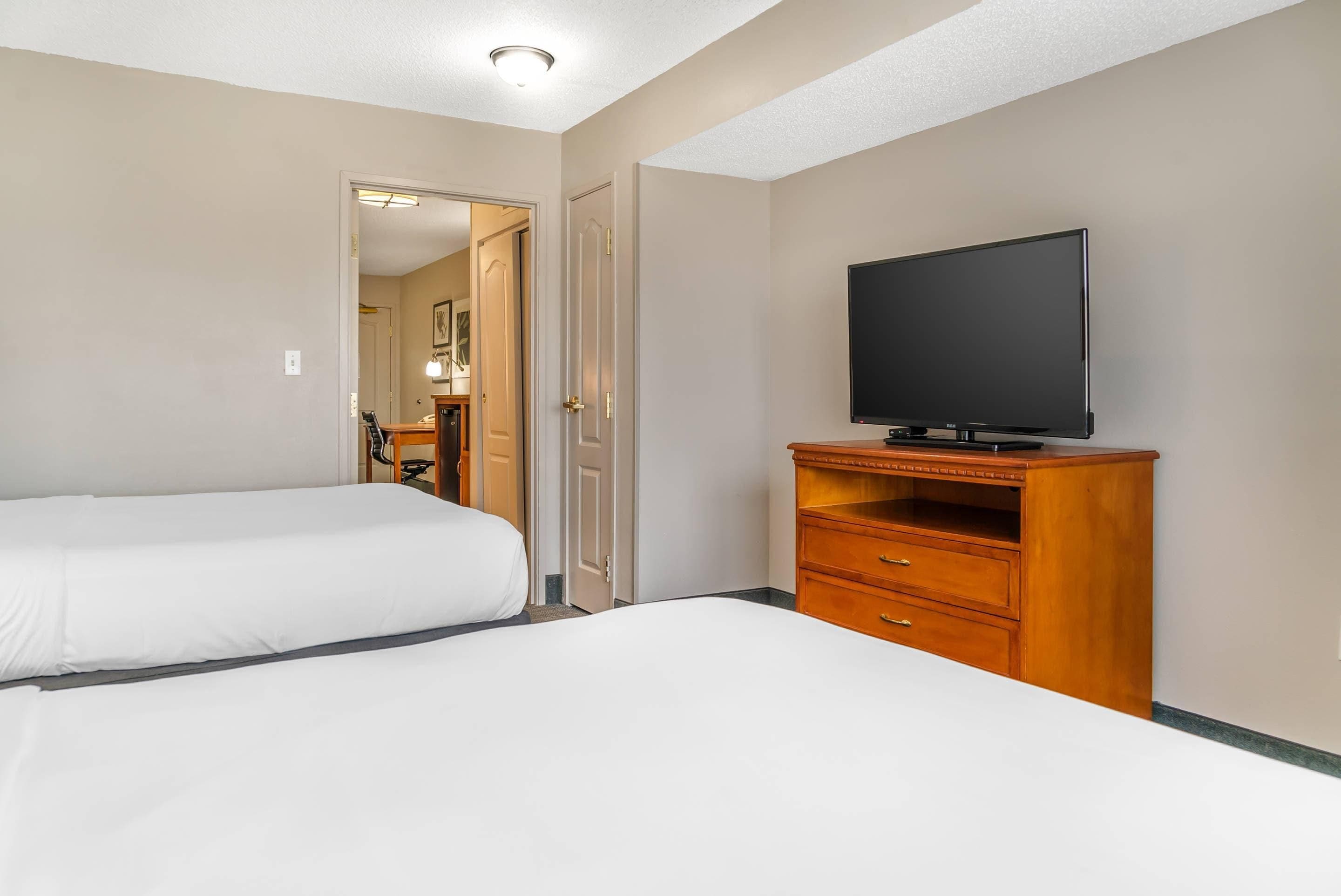 Een hotelkamer met twee bedden, een televisie op een houten standaard en een deur naar de badkamer.