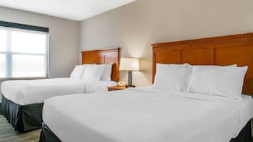 A hotel room with two beds, a nightstand with a lamp, and a window with blinds.