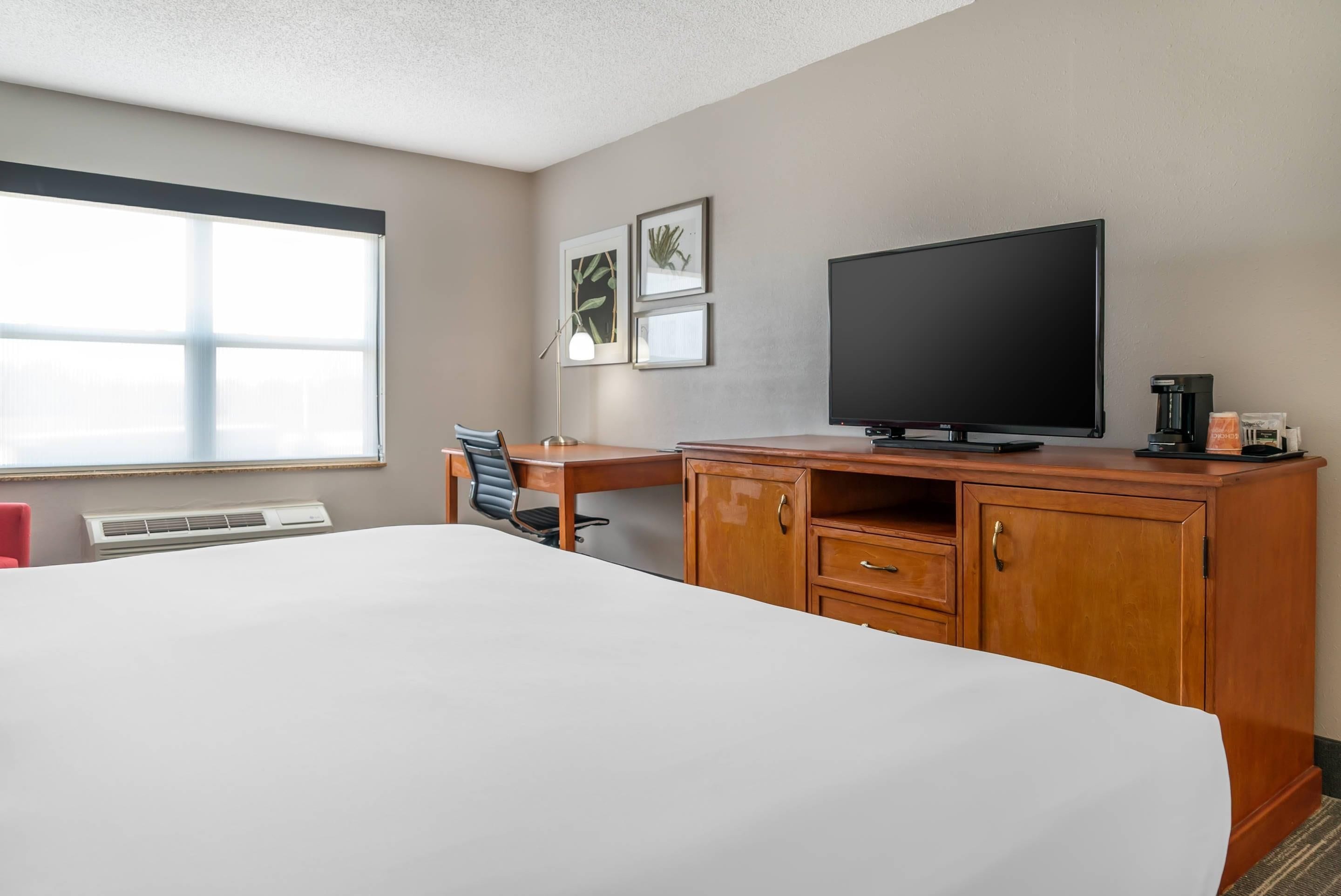 A hotel room with a bed, a desk, a television, and a coffee maker.