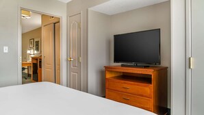 A bedroom with a bed, a wooden dresser, a television, and a door leading to a bathroom.