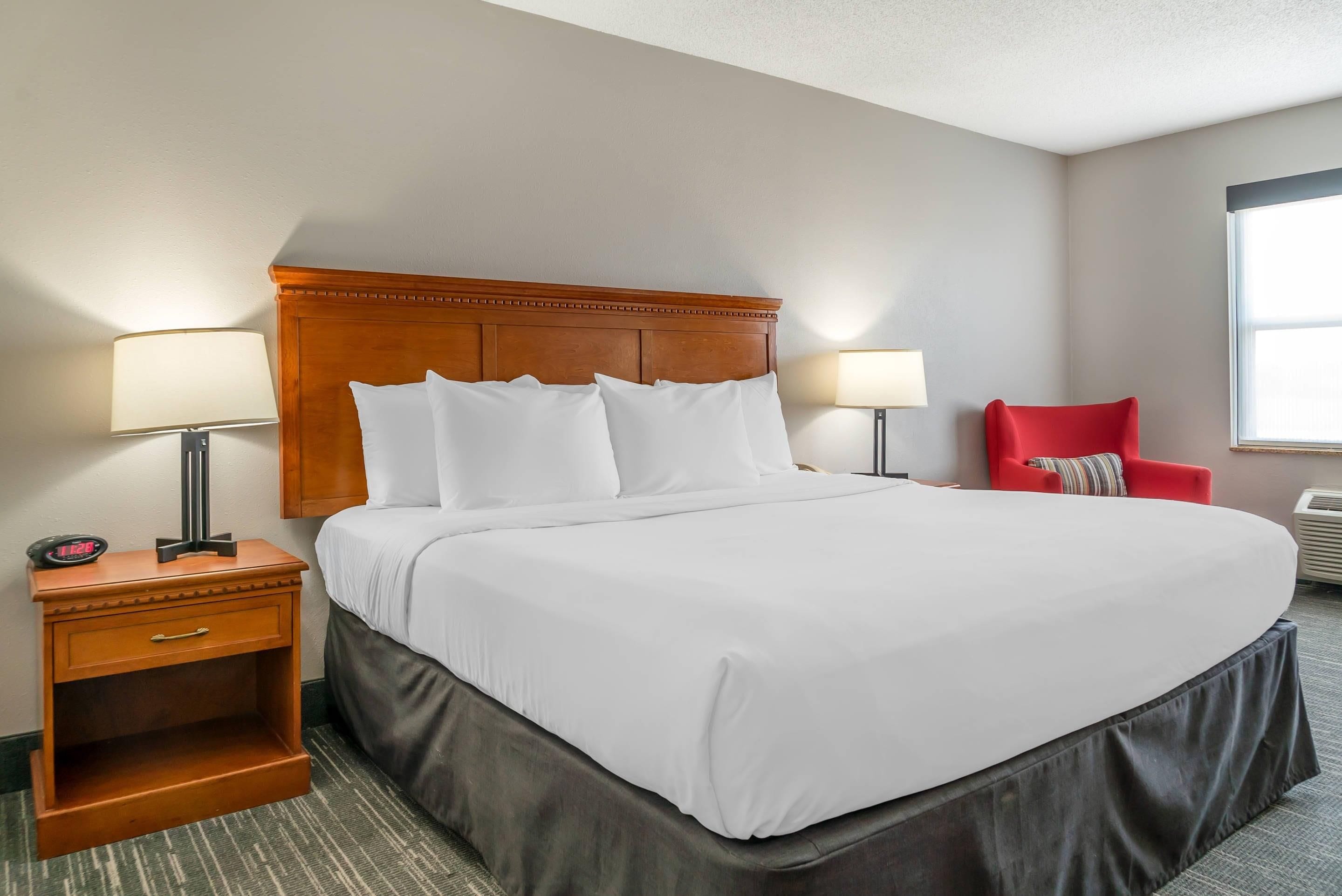 Ein Hotelzimmer mit einem Bett, zwei Nachttischlampen, einem roten Sessel und einer digitalen Uhr.