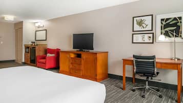 A hotel room with a bed, a desk, a chair, a television, a wardrobe, and artwork on the wall.