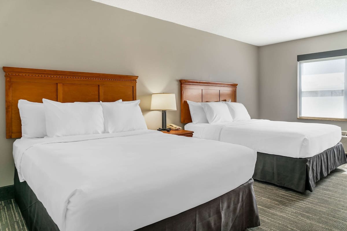 A hotel room with two beds, each with a wooden headboard, white bedding, and a bedside table with a lamp and phone.