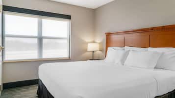 A hotel room with a large bed, a nightstand with a lamp, and a window with blinds.