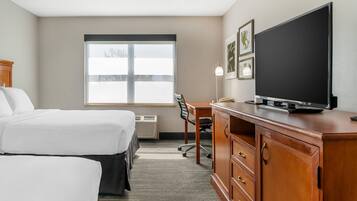 A hotel room with two beds, a desk with a flat-screen TV, a chair, and a window with blinds.