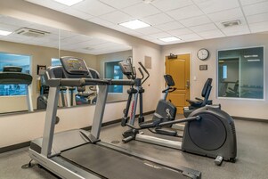 Un gimnasio con máquinas de cardio, un espejo grande y un reloj.