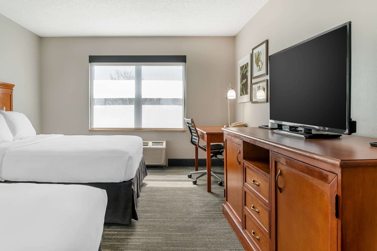 A hotel room with two beds, a desk, a television, and a window with blinds.