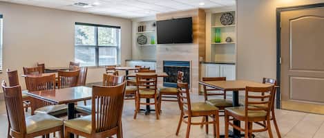 A dining area with multiple tables and chairs, a flat-screen TV mounted on the wall, and a fireplace.