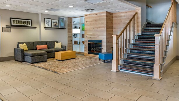 A spacious living area with a sofa, ottoman, and a fireplace. A staircase with wooden railings leads to an upper floor.