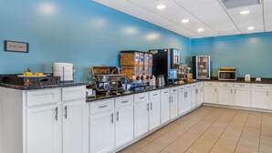 A clean, well-lit kitchen area with white cabinets, a blue wall, and various appliances like a coffee machine and microwave.