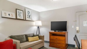 A room with a sofa, a red chair, a TV on a wooden stand, a lamp, and a door with a lock.
