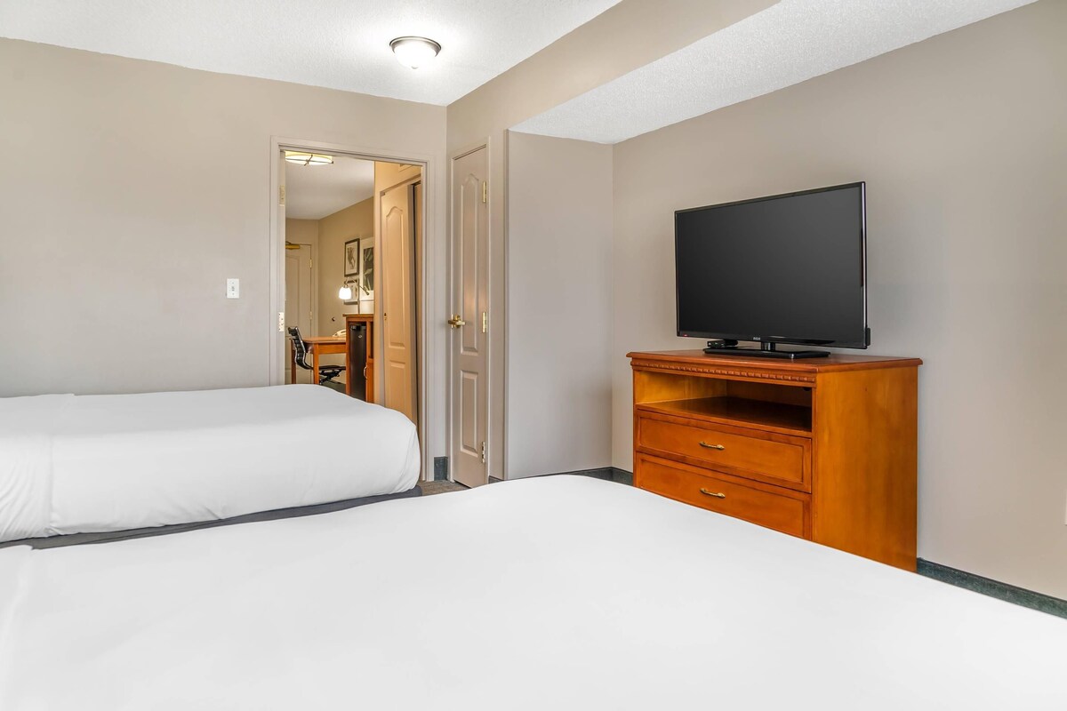 Une chambre d’hôtel avec deux lits, un téléviseur posé sur un meuble en bois et une porte donnant sur une salle de bain.