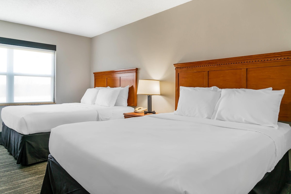 Une chambre d’hôtel avec deux lits, une table de chevet avec une lampe et une fenêtre.