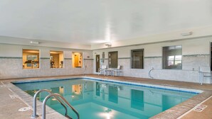 An indoor swimming pool with clear water, a metal ladder, and tiled walls.