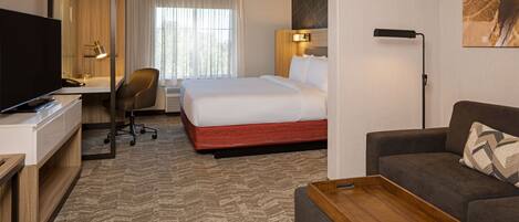 A hotel room with a bed, a desk with a TV, a chair, a sofa, and a wooden tray.