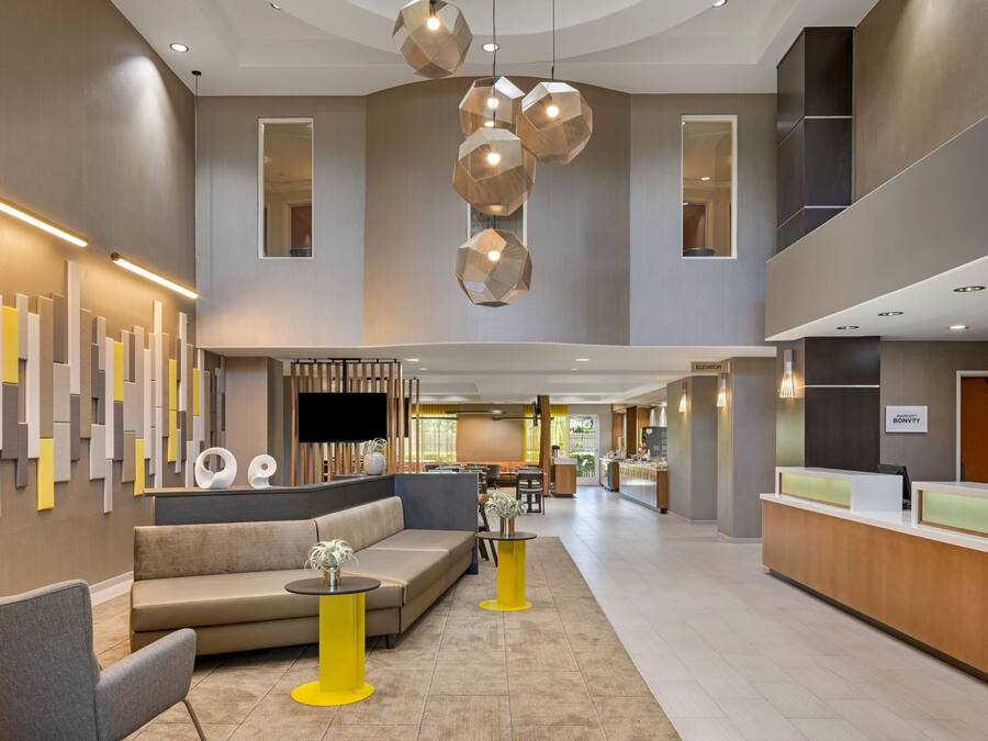 A modern hotel lobby with a reception desk, seating area, and a large window.