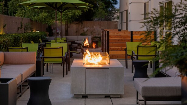 Ein Außenbereich mit Terrasse, Feuerstelle, Sitzgelegenheiten und Sonnenschirmen.