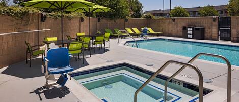 A swimming pool with a diving board, surrounded by green and blue lounge chairs and umbrellas.