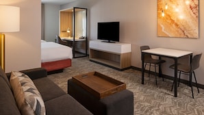 Ein Hotelzimmer mit Bett, Schreibtisch, Fernseher, Sessel, Sofa und Serviertisch.