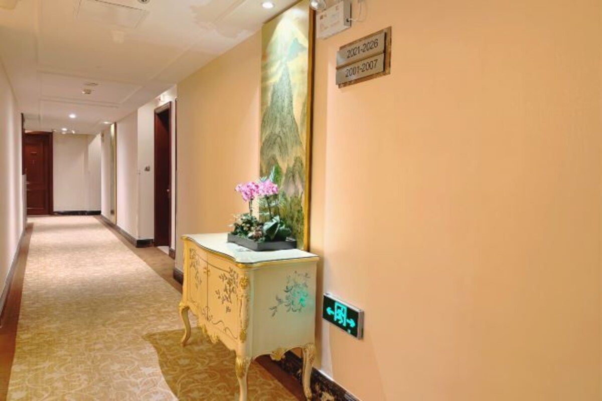 A hallway with a carpeted floor, a decorative console table with a vase of flowers, and a sign indicating room numbers.